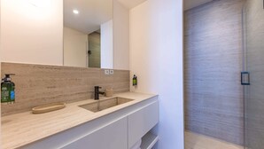 A modern bathroom with a large mirror, a sink, and a shower area.