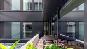 A modern building exterior with large windows, a balcony with wicker furniture, and potted plants. - Opera - Two Bedroom Balcony (Paris)