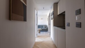 En smal hall med ett köksutrymme på höger sida, en soffa längre in i rummet och en dörr som leder till ett annat rum.