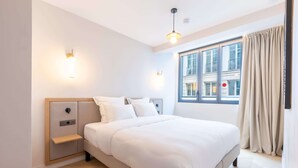 A modern hotel room with a large bed, bedside tables, wall-mounted lights, and a window with curtains. - Opera - One Bedroom in Paris (Paris)