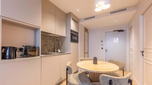 A modern kitchen with built-in appliances, a round dining table with chairs, and a door with a poster. - Opera - One Bedroom in Paris (Paris)