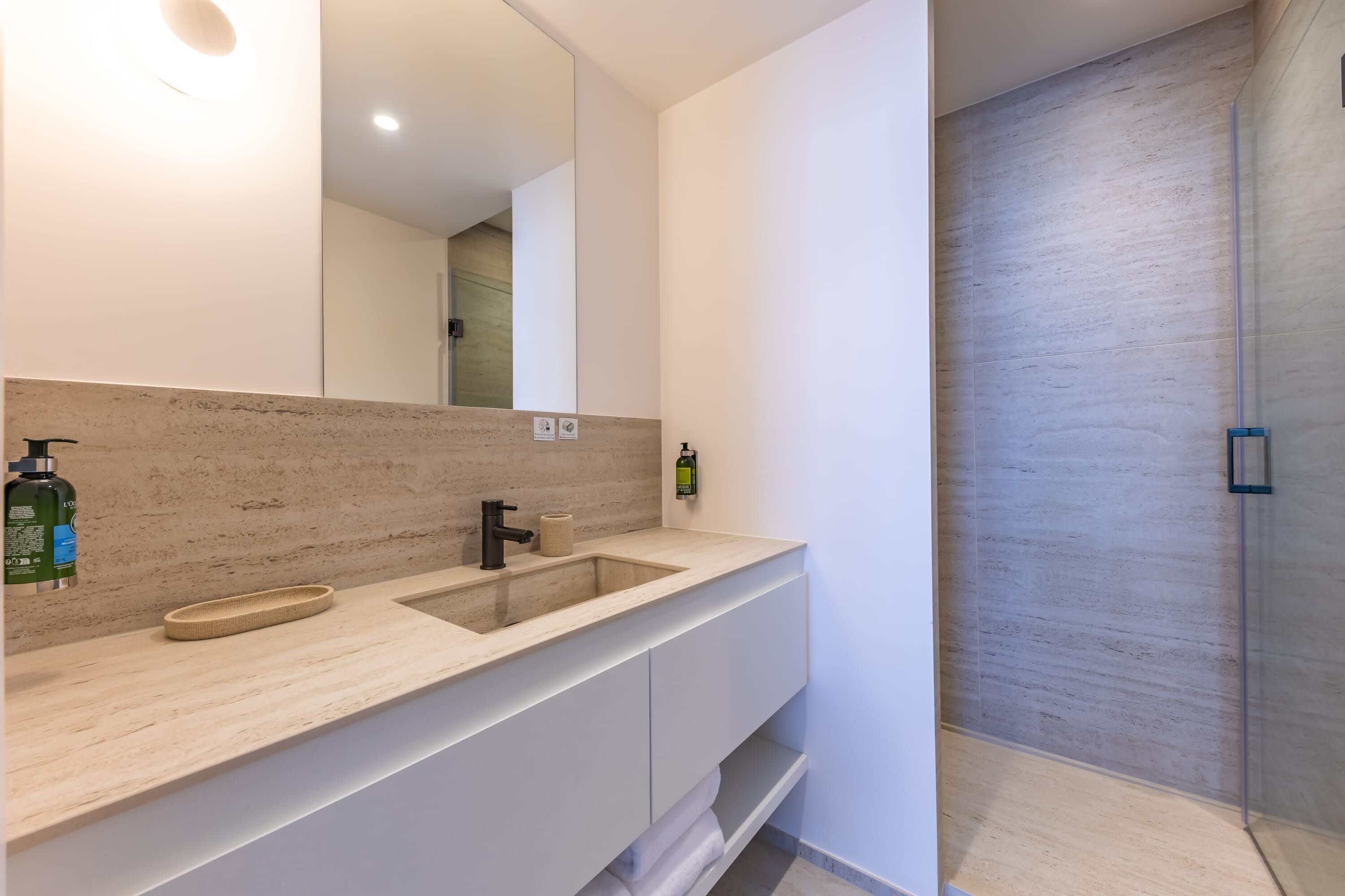 Un baño moderno con un espejo grande, un lavabo y una zona de ducha.
