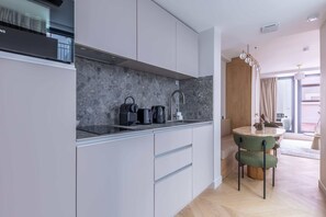 A modern kitchen with a marble backsplash, a built-in stove, and a sink. There is a dining area with a round table and chairs.