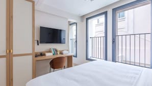 A hotel room with a bed, a desk, a chair, a television, and large windows.