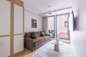 A modern living room with a sofa, a coffee table, a TV mounted on the wall, and a sliding glass door leading to an outdoor area.