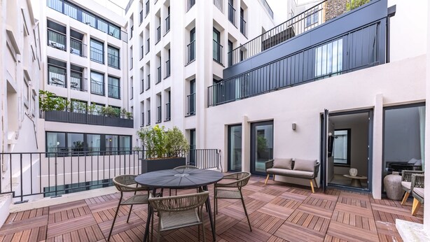 A courtyard with a round table and chairs, a sofa, and a potted plant.