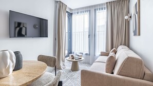 Een moderne woonkamer met een bank, een ronde salontafel en een aan de muur bevestigde televisie.