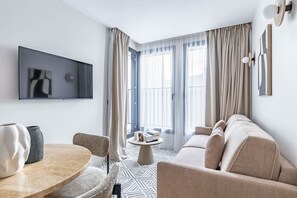 Een moderne woonkamer met een bank, een ronde salontafel en een aan de muur bevestigde televisie.