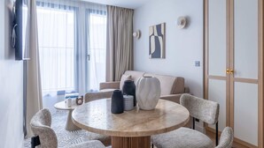 Een moderne woonkamer met een ronde salontafel, een beige bank en een aan de muur bevestigde televisie.