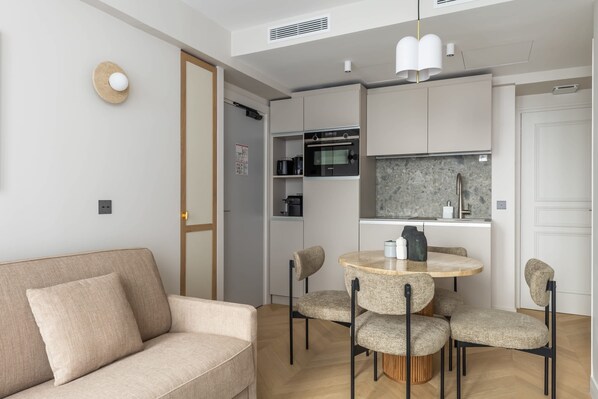 Eine moderne Küche mit integrierten Geräten, ein Essbereich mit rundem Tisch und Stühlen sowie ein Sofa im Wohnbereich.