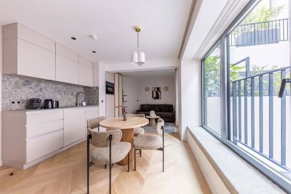 A modern kitchen with white cabinetry, a dining area with a round table and chairs, and a large window with a balcony view.