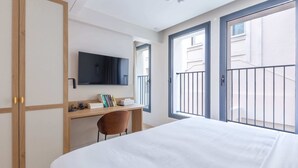 Une chambre d’hôtel équipée d’un lit, d’un bureau, d’une chaise, d’une télévision et de grandes fenêtres.