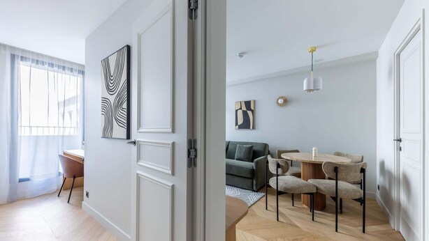 Una sala de estar moderna con sofá, mesa de comedor y sillas, una escalera y un ventanal.