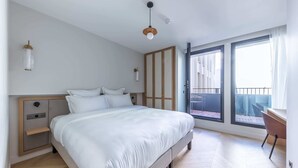 Un dormitorio con cama, mesitas de noche, armario, escritorio y balcón.