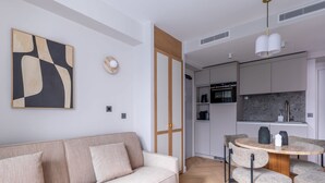 A modern living room with a sofa, a dining table with chairs, a kitchen area with cabinets, and a pendant light.