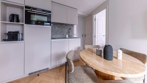 A modern kitchen with built-in appliances, a dining area with a round table, and a door leading to another room.