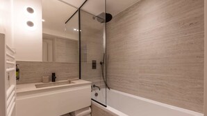 A modern bathroom with a glass-enclosed shower, a white vanity with a mirror, and a bathtub.