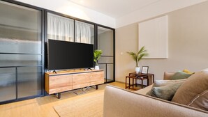 A modern living room with a large flat-screen TV, wooden entertainment unit, and a comfortable sofa.