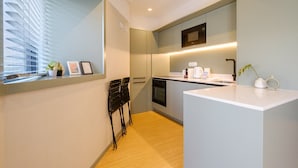 A modern kitchen with a built-in oven, a microwave, and a coffee maker on the countertop. There is a window with blinds and a small plant on the windowsill.