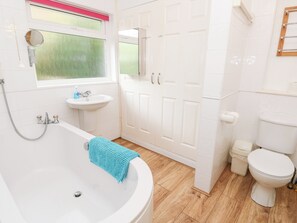 Ein Badezimmer mit Badewanne, Waschbecken, Toilette und einer Tür mit Spiegel.