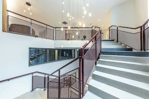 Espacio interior de varios niveles con escalera, barandales de metal y lámparas colgantes.