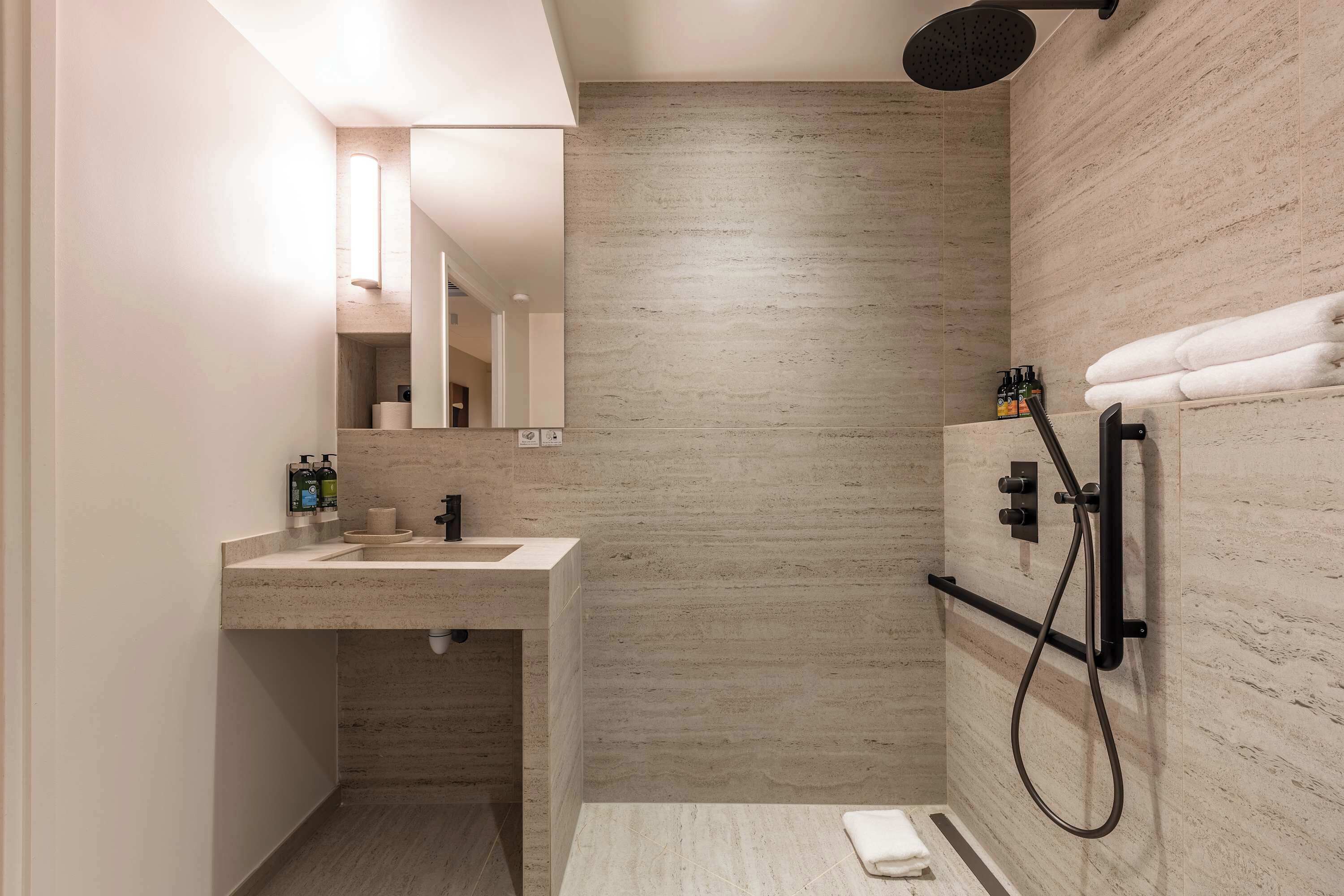 Un baño moderno con lavamanos, espejo, toallero y ducha.