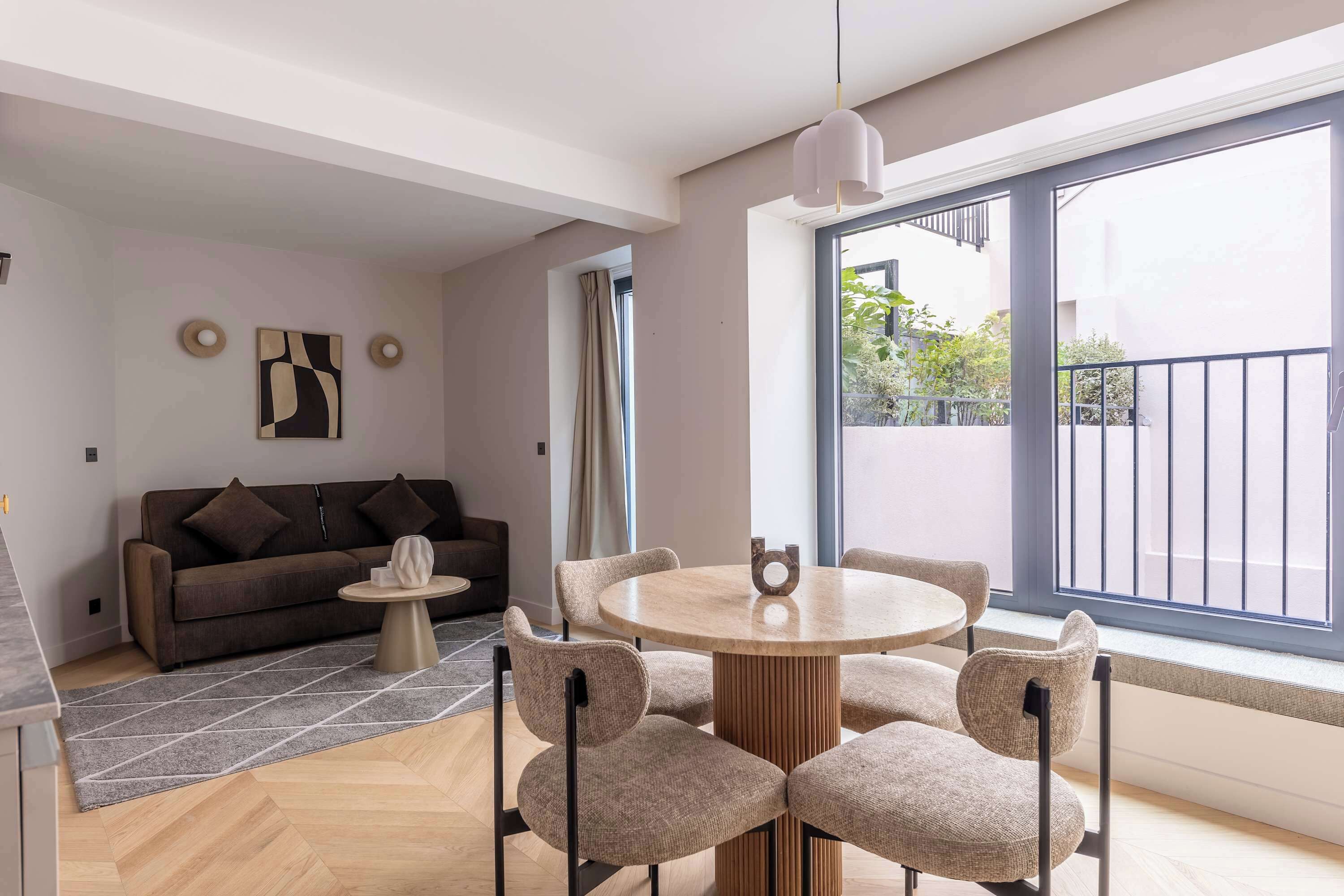 Ein modernes Wohnzimmer mit einer Couch, einem runden Tisch mit Stühlen, einem Couchtisch und einem großen Fenster mit Ausblick.