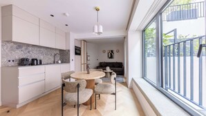 A modern kitchen with white cabinets, a round dining table, and chairs. There is a large window with a view of the outside. - Opera -3 Bedroom / 2 living rooms connecting apt. (Paris)