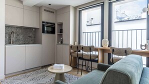 A modern kitchen with built-in appliances, a dining area with a sofa and chairs, and a large window with a view of buildings.