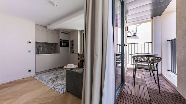 A modern kitchen with built-in appliances, a dining area with a round table and chairs, and a balcony with a railing.
