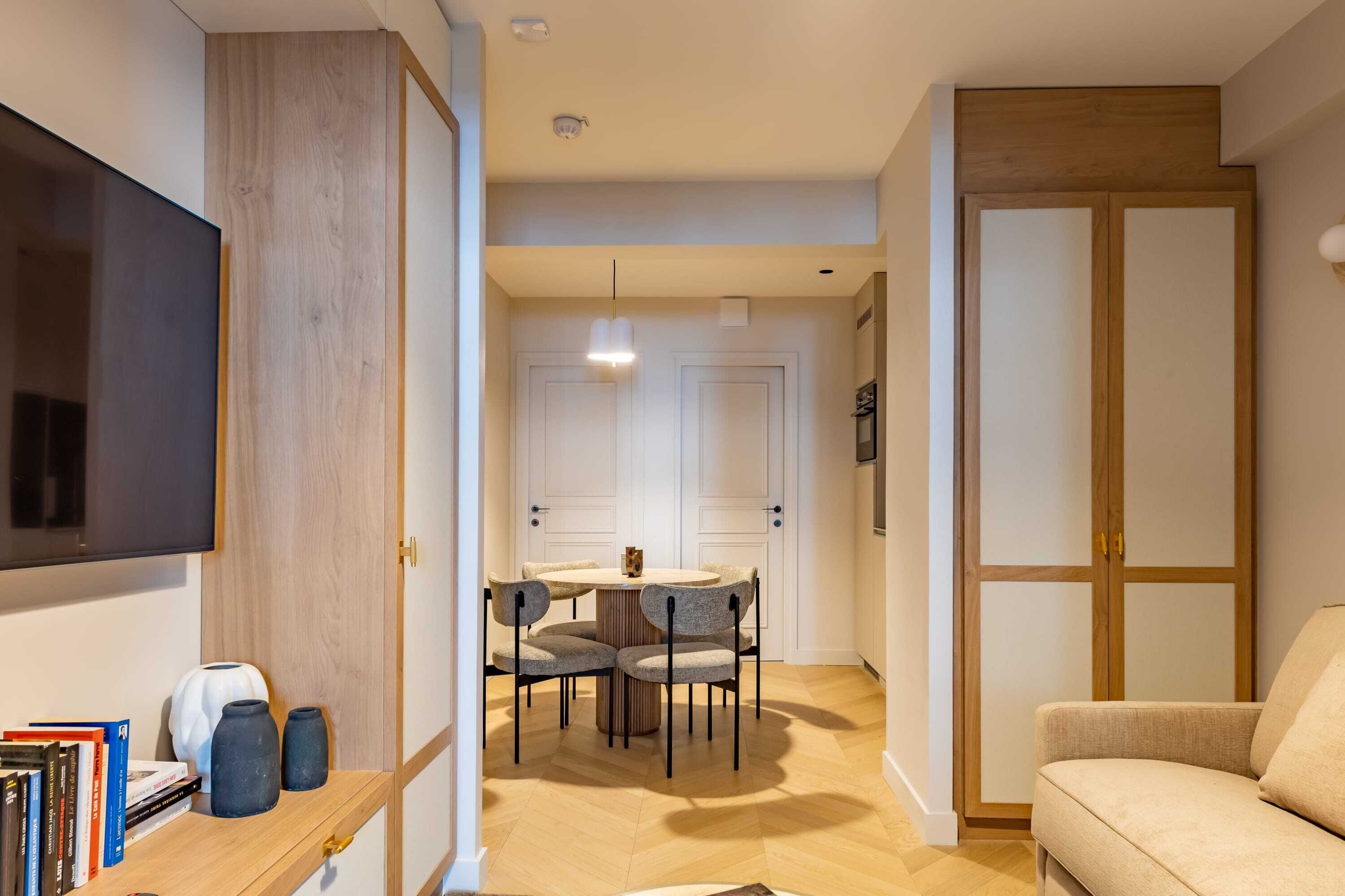 Una sala de estar moderna con un televisor de pantalla plana, una mesa de comedor redonda con sillas, un sofá y un armario de madera.