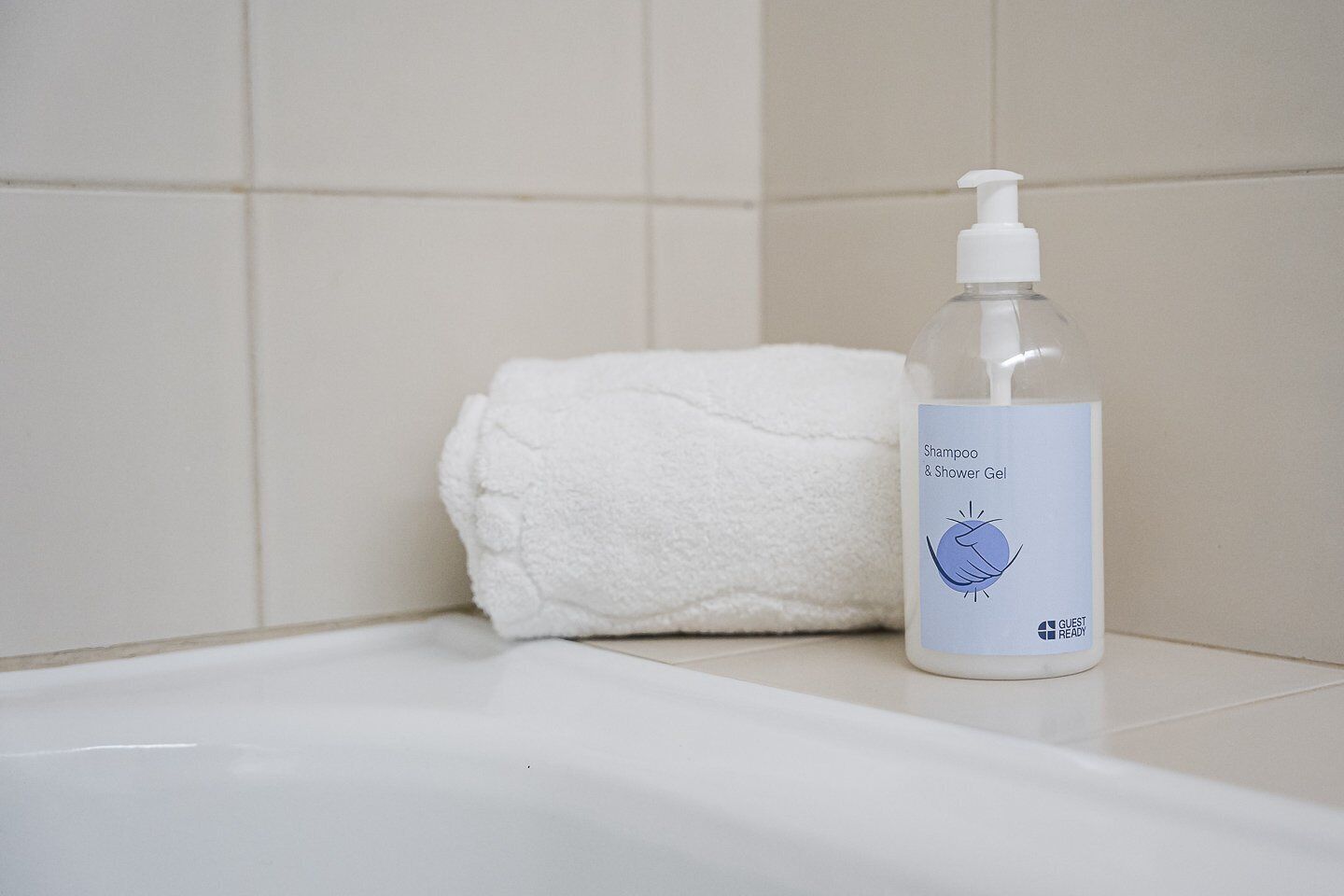A bathroom with a white bathtub, a white towel, and a bottle of shampoo and shower gel.