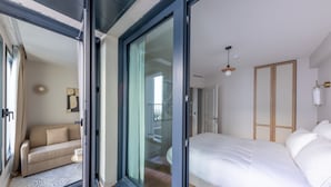Ein modernes Schlafzimmer mit einem großen Bett, einer Schiebetür zu einem Balkon und einem separaten Wohnbereich mit einer Couch.