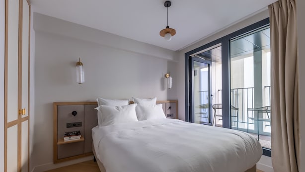 Ein modernes Hotelzimmer mit einem großen Bett, einem Nachttisch, einem Kleiderschrank und einem Balkon mit Gartenmöbeln.