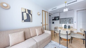 A modern living room with a sofa, a dining table with chairs, and a kitchen area in the background.