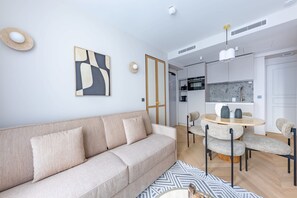 A modern living room with a sofa, a dining table with chairs, and a kitchen area in the background.