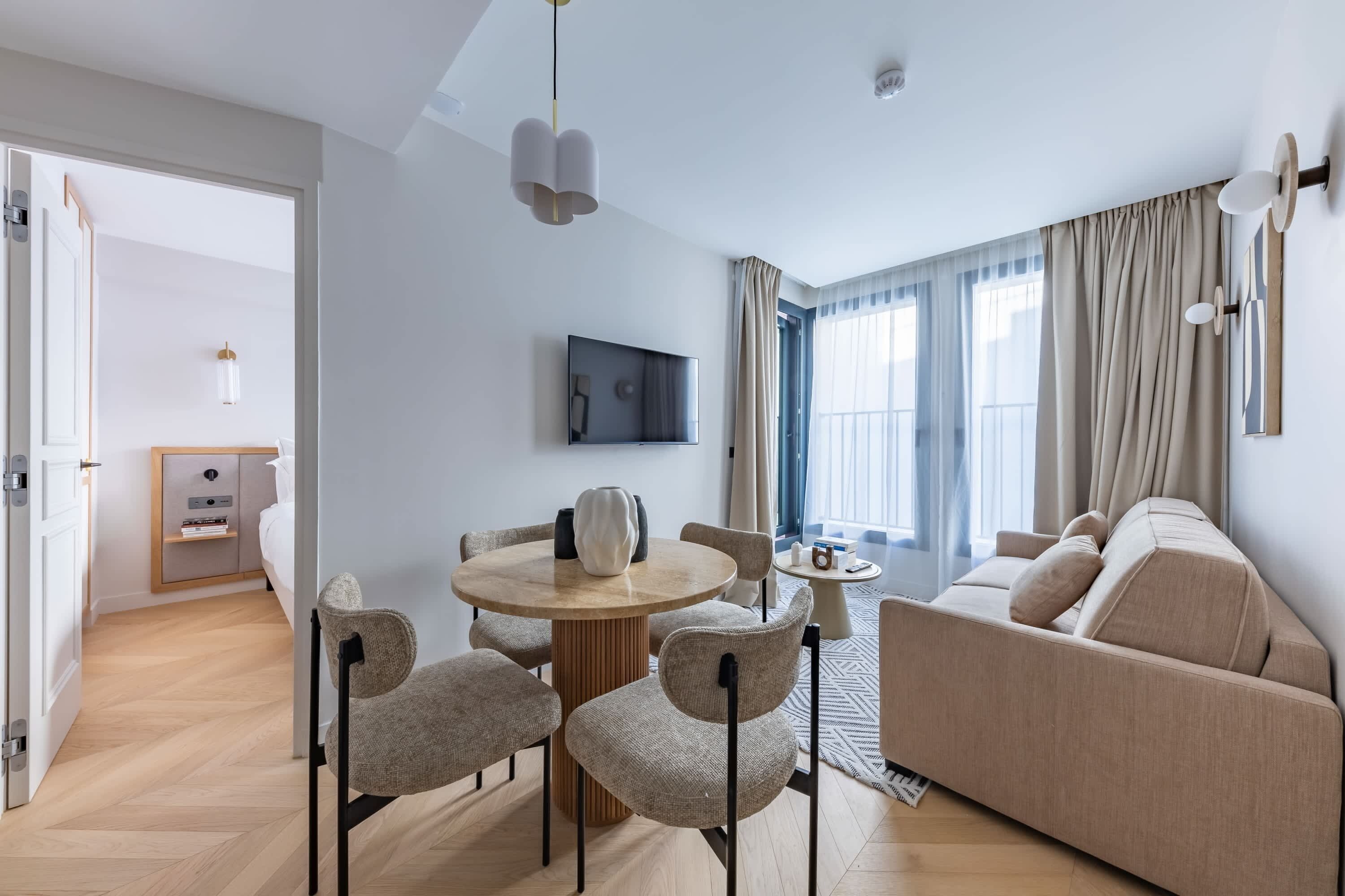A modern living room with a round dining table, sofa, and TV mounted on the wall.
