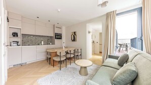 A modern living room with a sofa, a dining table with chairs, a kitchen area, and a balcony. - Opera - Two Bedroom Balcony (Paris)