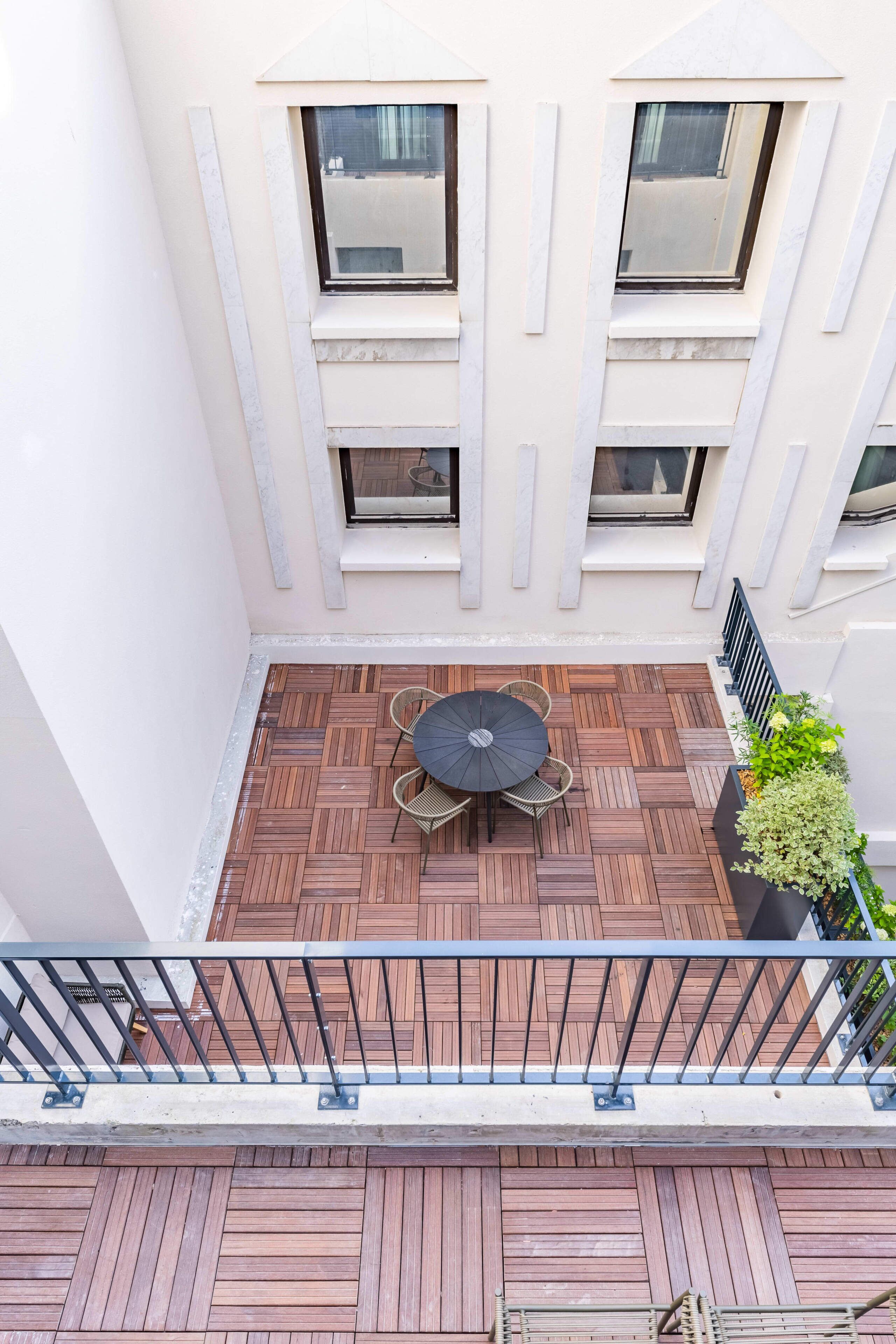 Een balkon op een hogere verdieping met een houten vloer, een ronde tafel met stoelen en een bloempot.