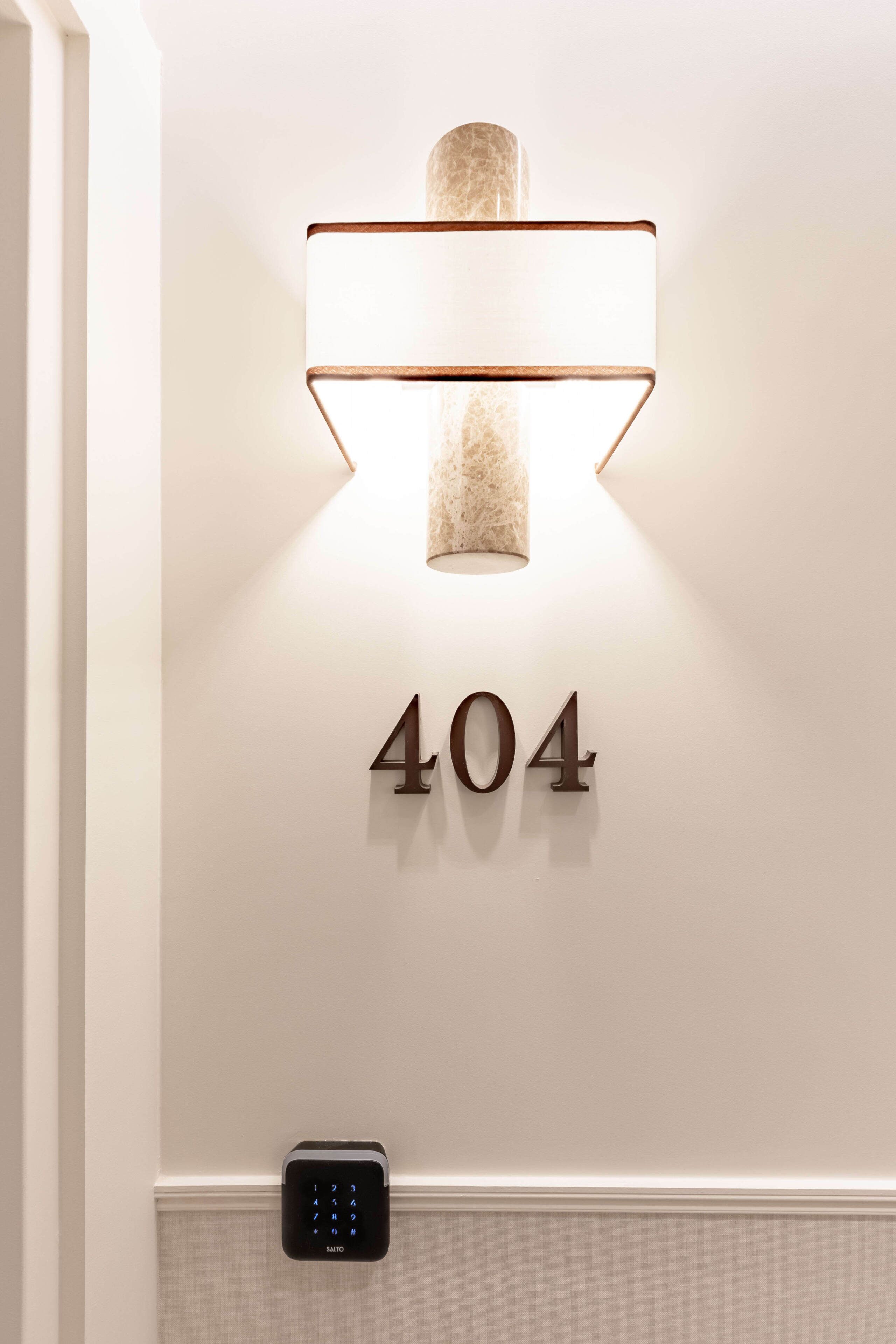 Una lámpara empotrada en la pared con el número '404' y un teclado debajo.