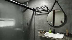 Une salle de bain moderne avec une douche à l’italienne en verre, des toilettes blanches, un lavabo sur un plan de travail en granit, un miroir rond et un porte-serviettes.