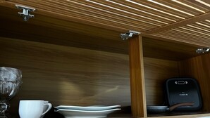 Un meuble en bois doté d’un couvercle à charnière, contenant une tasse blanche, une pile d’assiettes blanches et un appareil électronique noir.