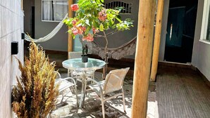 Un espace patio agrémenté d’une table ronde en verre et de chaises en osier, le tout entouré d’une pergola en bois.