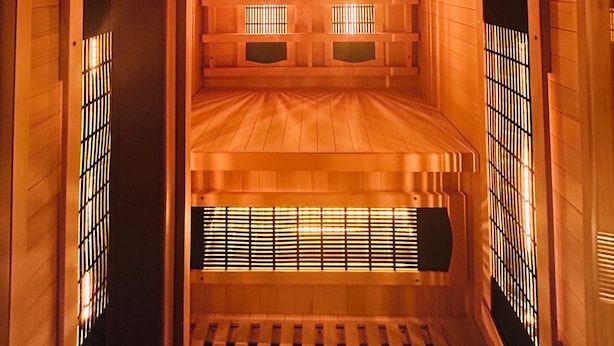 Un sauna avec des murs et des bancs en bois, un plafond doté de luminaires circulaires et un système de ventilation situé en bas.