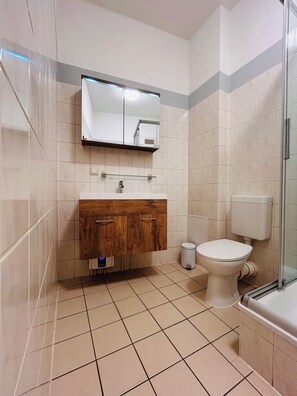 Ein Badezimmer mit einem Holzkosmetikschrank, einem Spiegel, einer Toilette und einer Duschkabine.