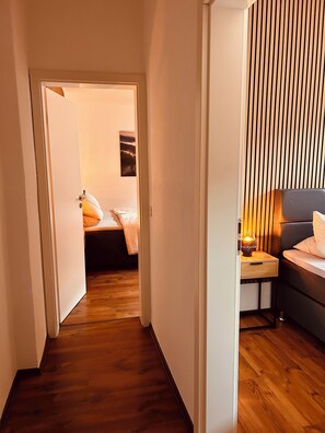 Ein schmaler Flur, der zu einem Schlafzimmer mit Bett, Nachttisch und Lampe führt.