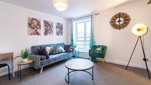 A modern living room with a grey sofa, a round coffee table, a green armchair, and a wall clock.