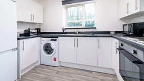 A compact kitchen with white cabinets, a built-in washing machine, a microwave, and a window providing natural light.