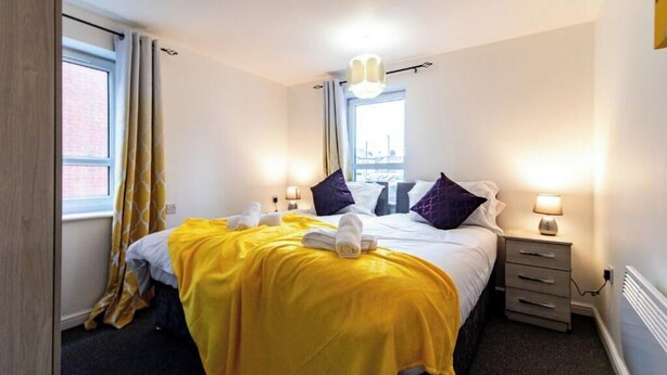 A hotel room with a bed, two bedside tables, a window with curtains, and a view of the city.