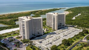 Ein Hochhaus-Hotel mit Parkplatz, umgeben von Grünflächen und Blick auf den Strand.
